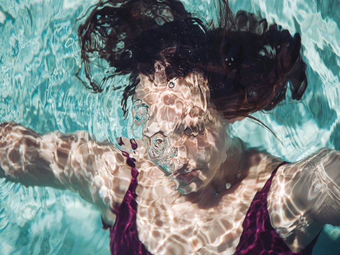 Woman floating underwater in a sunlit swimming pool