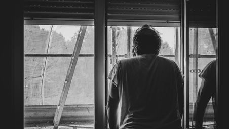 Person in a white shirt leans on a windowsill, gazing outside. Ladder visible through window. Monochrome, reflective, contemplative mood.