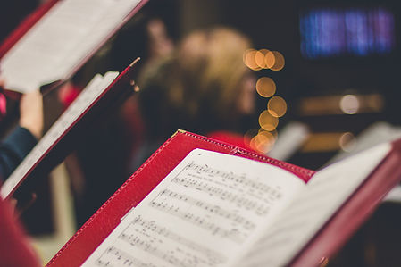 Red folders with sheet music in focus against a blurred background with warm lights and indistinct figures, creating a cozy ambiance.