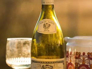 Wine bottle of Bourgogne Chardonnay with ornate label next to a decorative patterned cup and an empty glass, set on a wooden table.