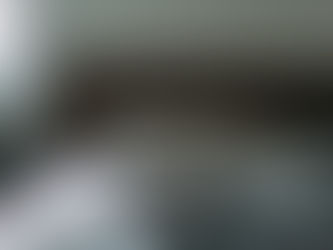 Unmade bed with gray patterned blanket and wooden headboard in a room with white shiplap paneled walls. Soft lighting suggests a calm mood.