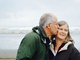Couple on a beach, with the husband kissing his wife's cheek
