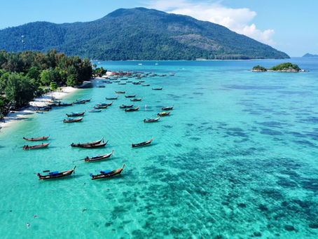 Mare cristallino punteggiato da imbarcazioni tipiche della Tailandia, ancorate vicino alla spiaggia