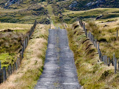 una strada di ghiaia corre in un paesaggio erboso in Irlanda con recinzione con pali di legno e fil di ferro ai lati della strada
