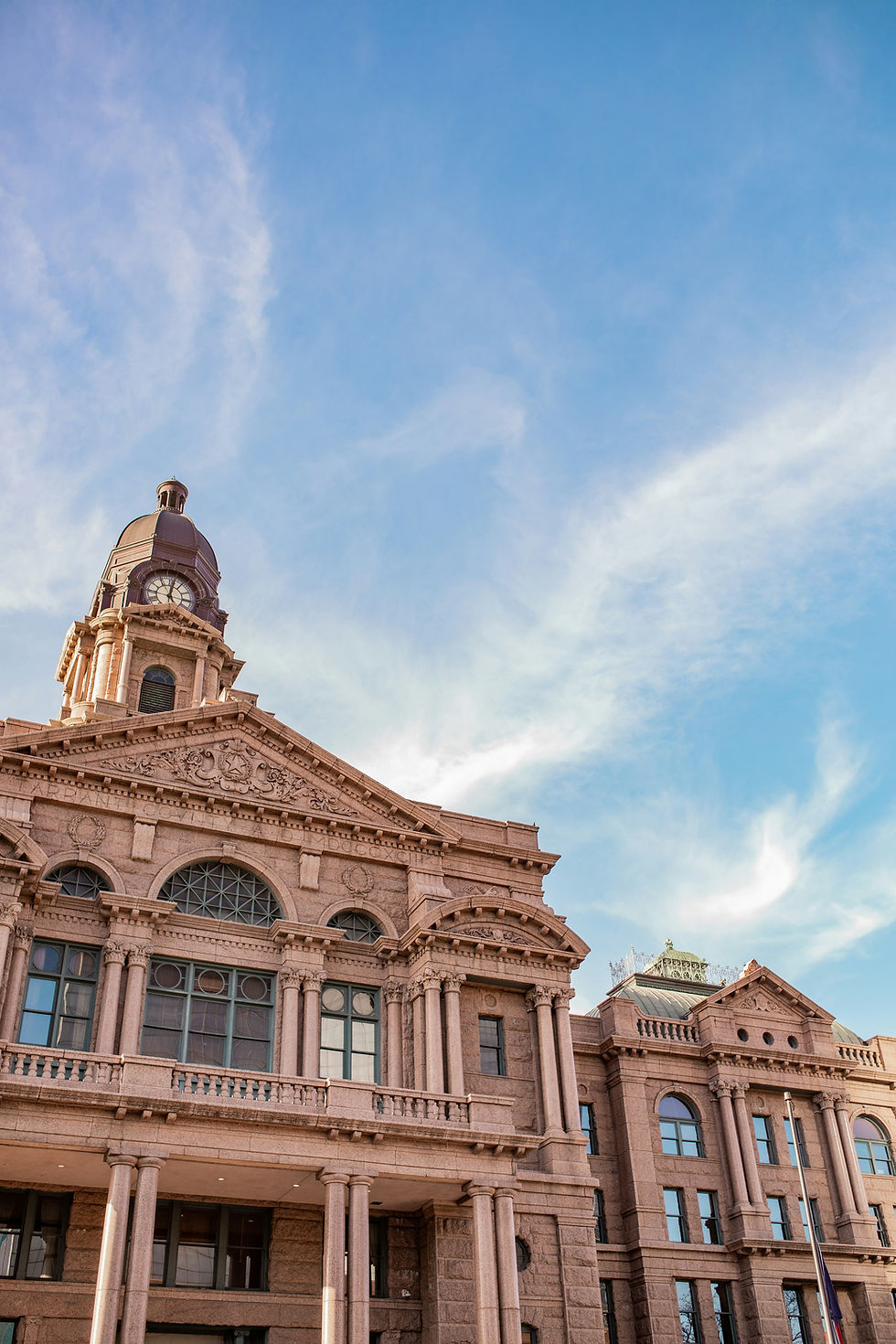 Historic stone courthouse with clock tower under a bright blue sky, seen from below; grand and stately.