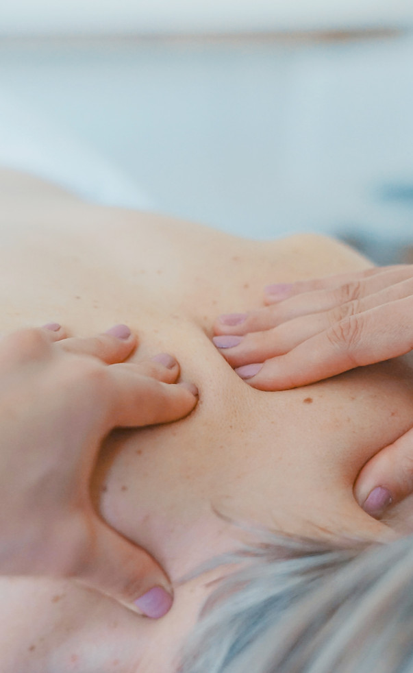 Person receiving a back massage by a person with light pink nails. The background is light blue.