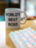 A coffee cup that says world's best boss sitting on a desk next to a computer keyboard