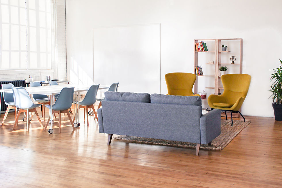 Bright room with a gray sofa, yellow chairs, blue chairs around a table, bookshelves, and a large window. Cozy and modern atmosphere.