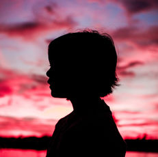 A young girl's silhouette framed against a pink sunset. 