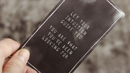 Hand holding a black card with white inspirational text that reads “Let your intuition guide you. You are what you’ve been looking for.” against a blurred gray background, symbolizing holistic healing and self-discovery.