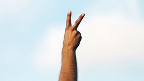 Hand making a peace sign against a clear blue sky background, conveying a sense of calm and positivity.