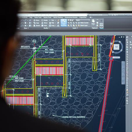 Person viewing architectural design on a computer screen with colorful lines and text. Office setting in the blurred background.
