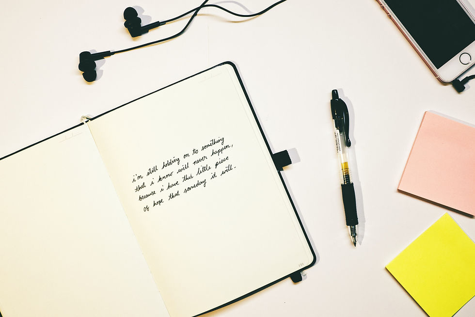Open notebook with handwritten text, black pen, earbuds, and pink and yellow sticky notes on a white surface. Calm, thoughtful mood.