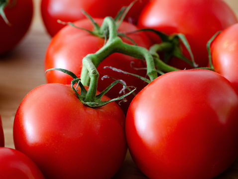 Fresh red tomatoes with green stems on a wooden surface, showing vibrant colors and a natural setting.
