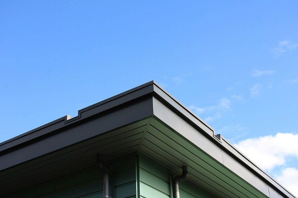 Modern building roof corner with dark trim and green siding against a bright blue sky with a few clouds