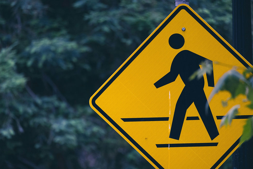 A man in a suit sits at a desk in a modern office, writing in a notebook with an open laptop in front of him.