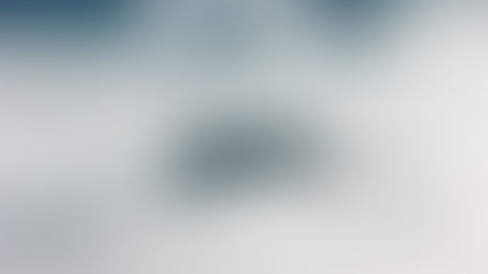 Mist-covered hills with a few lone trees rising above a sea of white fog under dark mountain ridges.