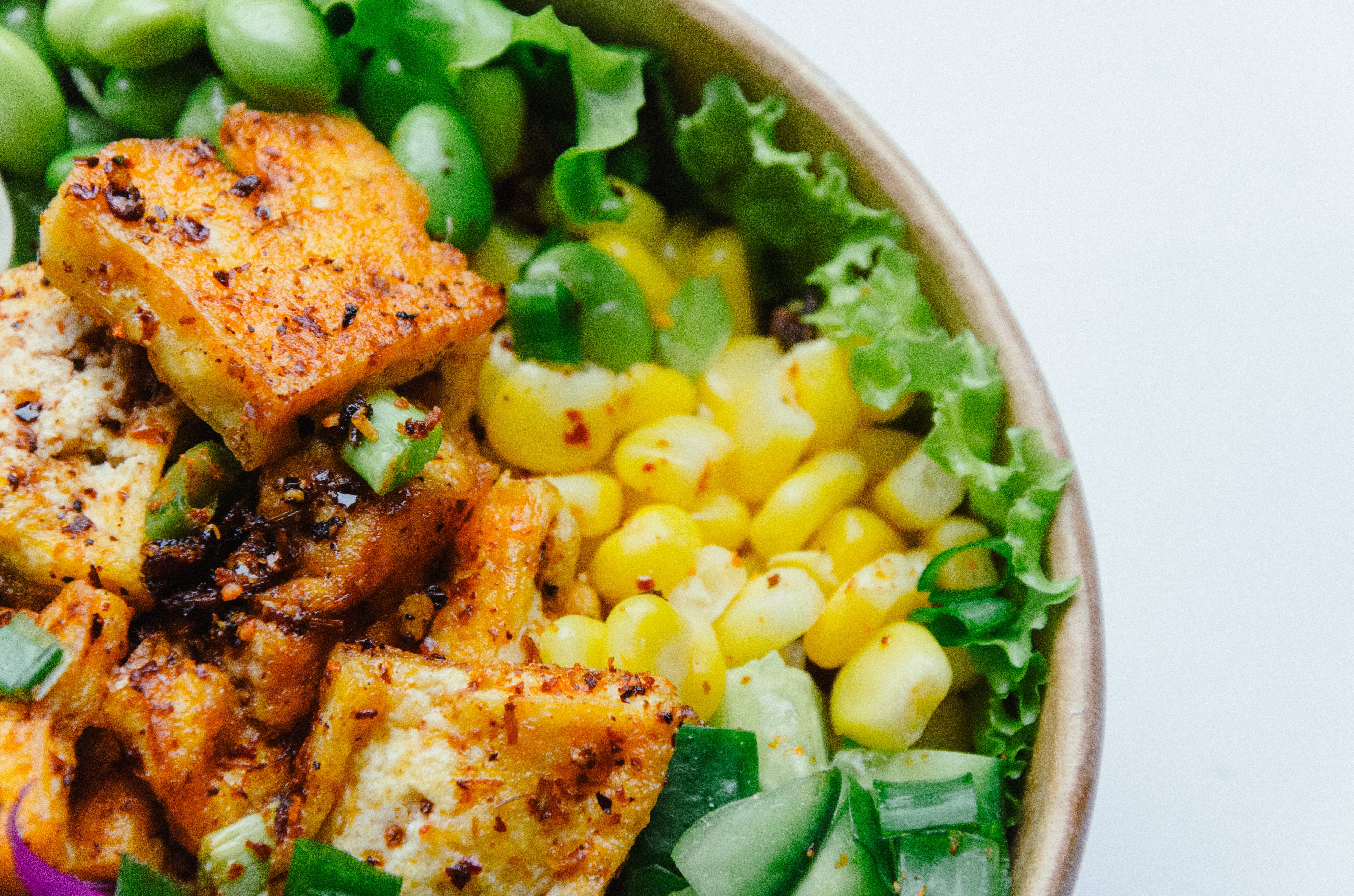 A bowl of seasoned tofu, corn, edamame, and fresh greens. The colors are vibrant, with a focus on yellows and greens.