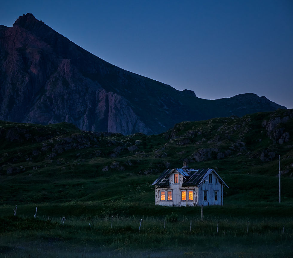 a single white house lit up at night by the mountain side