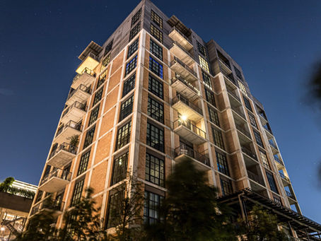 Tall brick building with balconies under a starry night sky, illuminated by warm lights. Trees at the base add a natural touch.