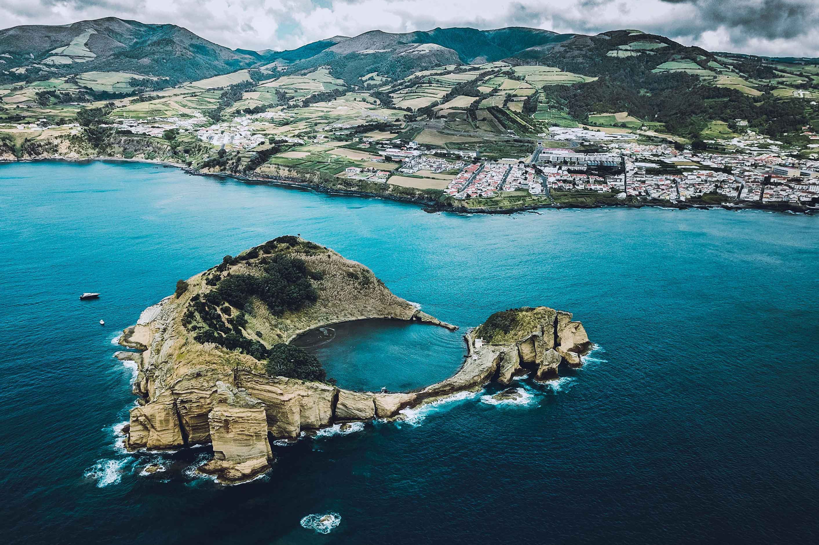 A breathtaking aerial view of the Azores, showcasing dramatic cliffs, a volcanic islet, and the lush countryside.