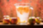 A jug of fruit infused water with whole apples on a table