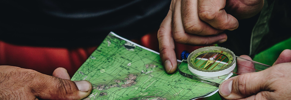 Close-up of two hands holding a topographic map and a compass, planning a route outdoors. The compass is being aligned with the map, indicating navigation or hiking activity.