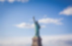 Daytime framing of the Statue of Liberty from a great distance. A clear sky in the background.