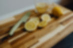 Sliced lemons and a whole lemon on a acacia wood board with a green-handled knife. A glass cup of lemon water in the background. Bright and fresh.