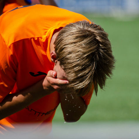 Frustrated young grassroots football player covering his face on the pitch after a tough match.