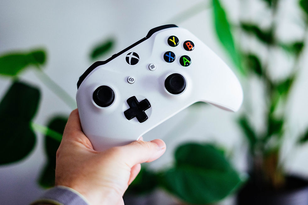 A white xbox controller being hold by a white hand behind some plants