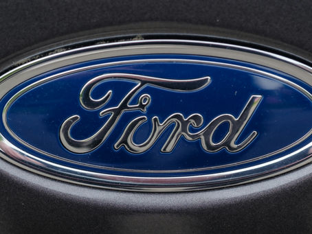 A close-up of a Ford logo on a car, featuring a blue oval with shiny silver lettering and trim, set against a smooth black surface.