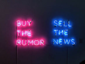 Pink and blue neon wall signs read BUY THE RUMOR and SELL THE NEWS on a dark background, creating a bold, edgy mood