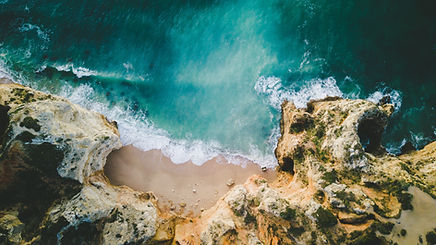 Aa aerial view of a amazing beach surrounded by rocks describing the region of western Algarve in the exclusive Algarve guide offered by the trusted realtor Lagos Homes in Portugal