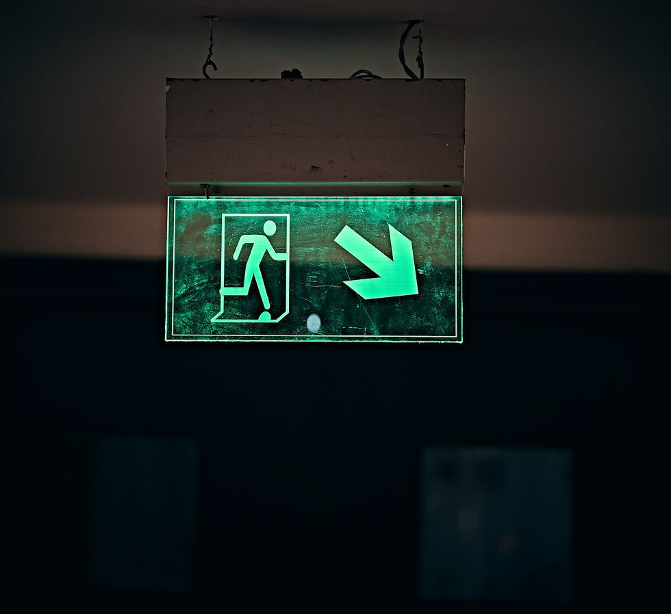 Illuminated emergency exit sign with a green glow, indicating the direction to safety with an arrow pointing downwards to the right.
