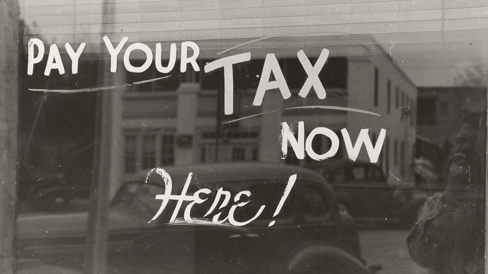 Black and white window with "Pay Your Tax Now Here!" text, reflecting cars and buildings, creating a vintage urban feel.