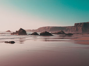Golden hour Atlantic coastline in Portugal with glowing surf, wide open sand, and dramatic light reflecting across the beach.