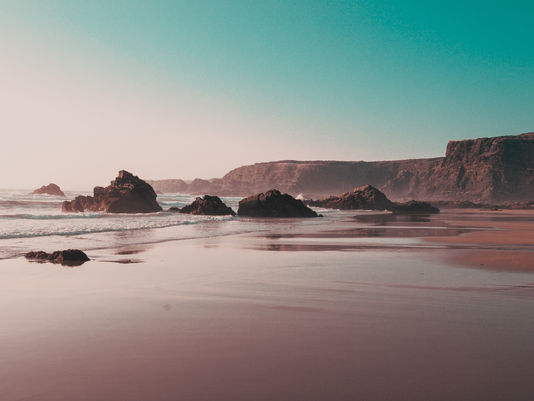 Golden hour Atlantic coastline in Portugal with glowing surf, wide open sand, and dramatic light reflecting across the beach.