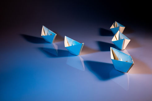Small paper sailing boats on a desk showing one boat out in front as the leader.