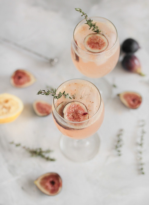 Two pink cocktails with fig and lemon garnish