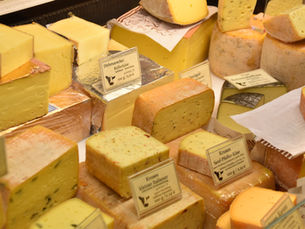 Assorted cheeses in a deli case with German price labels, stacked yellow and orange wedges under warm light.