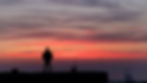 Silhouette of a person standing on a rooftop at sunset. Vibrant orange and pink clouds fill the sky, creating a dramatic and serene scene.