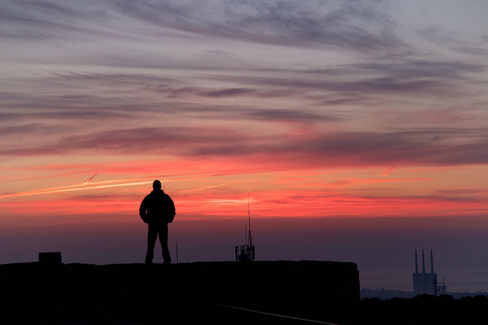 Silhouette of a person standing on a rooftop at sunset. Vibrant orange and pink clouds fill the sky, creating a dramatic and serene scene.