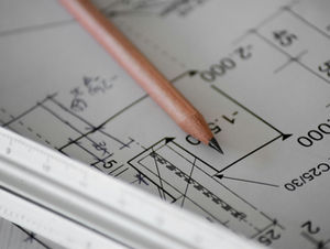 Pencil tip on an architectural blueprint with a ruler, showing measurements and line drawings in a focused work scene.