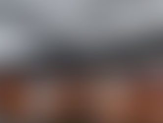 Colorful wooden houses line a waterfront against a mountain backdrop under cloudy skies. Warm reflections appear on the calm water.