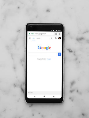 Smartphone displaying Google homepage on a white marble surface. The browser shows "https://www.google.com" with search bar.
