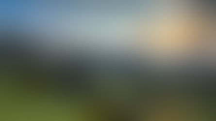 Misty green mountains and cliffs at sunrise, with a winding road below and golden clouds in a dramatic sky