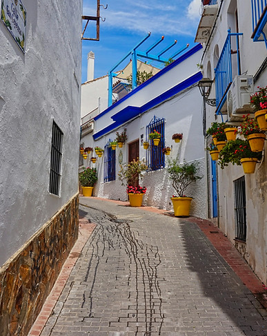 Charming cobblestone street in Spain lined with colourful buildings, flower-filled balconies, and warm Mediterranean light