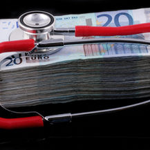 Red stethoscope resting on a stack of 20-euro banknotes on a black background, suggesting healthcare costs