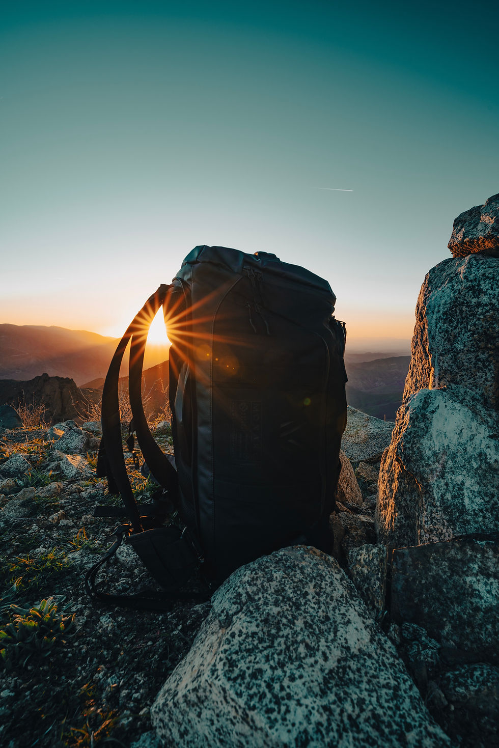 A backpack on a rocky hill with the sun setting behind it